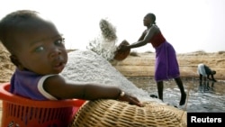 FILE - Mariama Diokh throws salt onto a pile while her 5-month-old infant sits nearby on the Senegal coast close to the Gambian border, June 2006. 