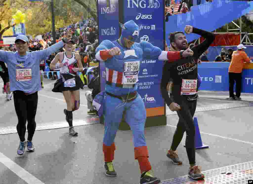 Runners, including a man wearing a Captain America costume, react as they cross the finish line after completing the New York City marathon, Nov. 3, 2013.