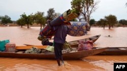 FILE - A man carries his belongings to a boat during flooding in a district in Niamey, Niger, Sept. 5, 2013. 