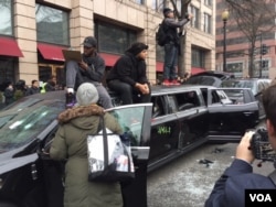 People gather around and on top of a vandalized limousine as Donald Trump is sworn-in as the 45th President of the United States in Washington, D.C., Jan, 20, 2017. (J. Swicord/VOA)