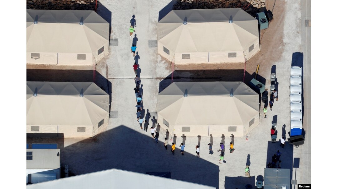 Niños inmigrantes, muchos de los cuales han sido separados de sus padres bajo una nueva política de "tolerancia cero" de la administración Trump, se muestran caminando en fila india entre tiendas de campaña en su recinto junto a la frontera con México en Tornillo, Texas, EE.UU.