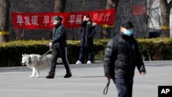 Residents wearing protective face masks walk by a propaganda banner which reads "Early detection, early reporting, early isolation and get early treatment" hangs on a neighborhood alley following the coronavirus outbreak in Beijing, Sunday, March 1, 2020.