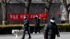 Residents wearing protective face masks walk by a propaganda banner which reads 