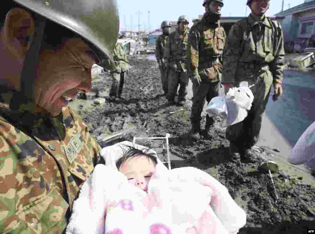 Солдат японских вооруженных сил держит на руках четырехмесячного младенца, спасенного вместе с семьей от наводнения в городе Ишимаки. 14 марта 2011 год