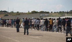 FILE - Italian border police escort sub-Saharan men on their way to a relocation center, after arriving in the Golfo Azzurro rescue vessel at the port of Augusta, in Sicily, Italy, June 23, 2017.