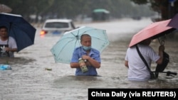 河南省郑州市的居民趟过齐腰洪水的街道。 （2021年7月20日）