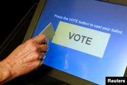 FILE - An elections official demonstrates a touch-screen voting machine at the Fairfax County Governmental Center in Fairfax, Virginia, Oct. 3, 2012.