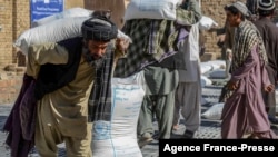 Afghan people carry sacks of food grains distributed as an aid by the World Food Program in Kandahar on Oct. 19, 2021. 