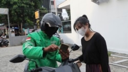 Indonesian journalist Ghina Ghaliya confirms an address with a delivery man before shipping used mobile phones to underprivileged children who lack internet access to study online, in Tangerang, Indonesia, on Sept. 25, 2020.