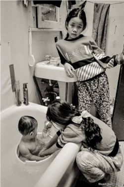 Two Cambodian sisters bathe their baby brother in an apartment building, in Uptown, Chicago.