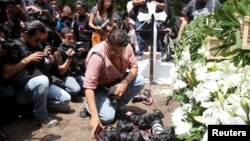 A photographer places his camera next to wreaths during the funeral service of late photojournalist Ruben Espinosa, at a cemetery in Mexico City, Aug. 3, 2015. 