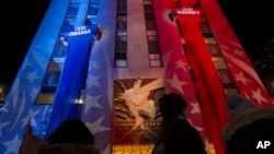 People watch early election results displayed on a utility lift suspended from the front of the GE Building at Rockefeller Center New York, Tuesday, Nov. 6, 2012.