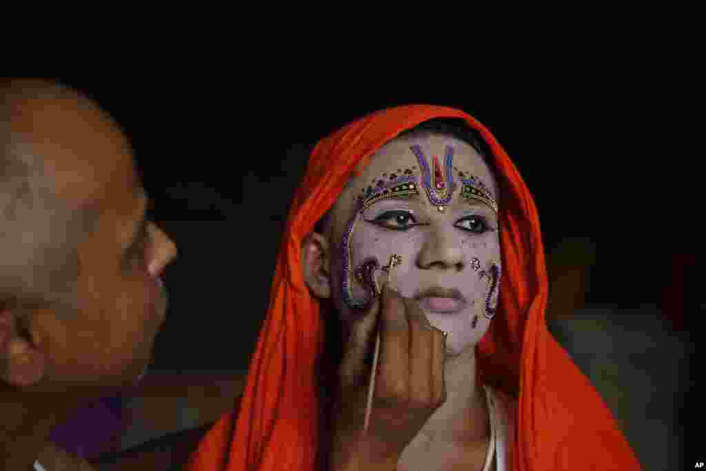 A man puts on makeup on an artist dressing up as Hindu god Rama ahead of a religious procession during the Dussehra festival in Allahabad, India.