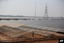 FILE - An official walks past solar panels at the Pavagada Solar Park, 175 kilometers (109 miles) north of Bangalore, India, March 1, 2018. The park is expected to produce 2,000 megawatts of power.