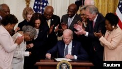 U.S. President Joe Biden is applauded as he reaches for a pen to sign the Juneteenth National Independence Day Act into law as Vice President Kamala Harris stands by in the East Room of the White House in Washington, U.S., June 17, 2021. REUTERS/Carlos Ba