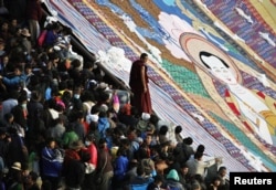 A Tibetan Buddhist monk stands between tourists and a giant thangka, a religious silk embroidery or painting unique to Tibet, during the Shoton Festival at Drepung Monastery on the outskirts of Lhasa, Tibet Autonomous Region, August 29, 2011.