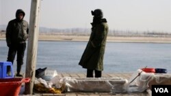 中國漁民在丹東的河邊賣魚，河對岸是朝鮮邊境城鎮新義州。(2013年2月7日) 