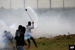 A Palestinian demonstrator uses a sling to hurl back a tear gas canister fired by Israeli forces during a protest marking Land Day and the first anniversary of a surge of border protests, at the Israel-Gaza border fence east of Gaza City, March 30, 2019.
