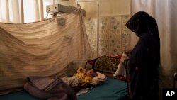FILE - A woman changes the clothes of her baby in the malnourished ward of the Mohammed Khan Hospital in Sayedabad district, Wardak province, Afghanistan, Oct. 11, 2021.