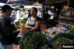 A vendor talks with a customer in her fruit and vegetables stall selling medicines at a market in Rubio, Venezuela, Dec. 5, 2017.