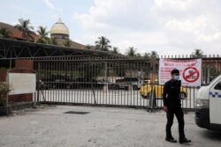 Polisi yang mengenakan masker menjaga masjid Seri Petaling di Kuala Lumpur, Malaysia yang kini ditutup untuk sementara (18/3).