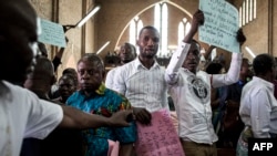 Quelque personnes brandissent des affiches lors d'une messe en mémoire des victimes de la répression de la marche du mois dernier à Kinshasa, le 12 janvier 2018.