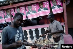 A customer checks sugar cane sold by a street vendor next to posters of presidential candidate Jovenel Moise of PHTK (Bald Head Haitian Party) before the election in a street of Les Cayes, Haiti, Nov. 19, 2016.