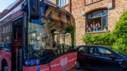 A group of people wave from a window as a bus delivers a loudspeaker message from family and friends in Brussels, Wednesday, April 22, 2020. (AP Photo/Olivier Matthys)