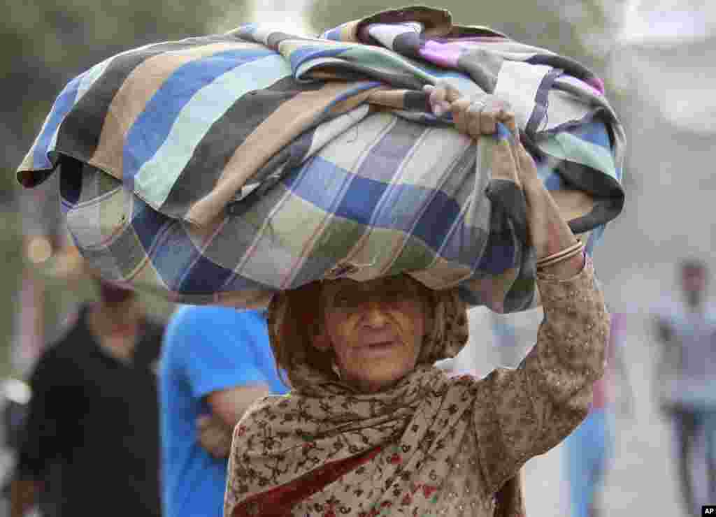 An old Indian villager from the Indian side of the border between India and Pakistan, carries her belongings to a relief camp set up at a government run school in Akhnoor, about 55 kilometers north of Jammu, India.