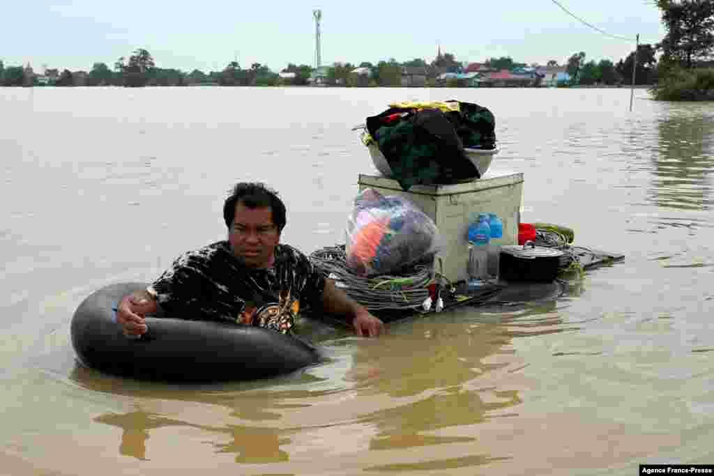 A man makes his way through floodwaters to carry goods on the outskirts of Phnom Penh, Cambodia, following heavy rains.
