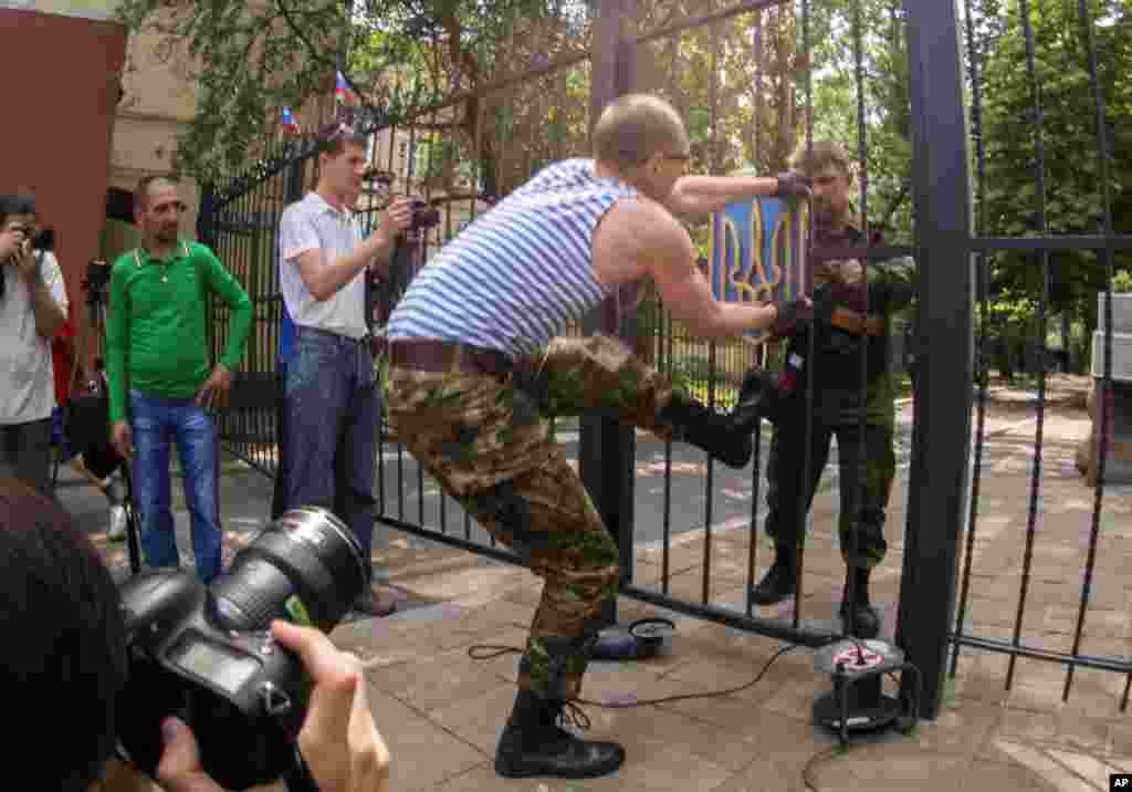 A pro-Russian man tries to remove a Ukrainian national emblem from the gates to the city administration headquarters in Luhansk, Ukraine, June 9, 2014. 