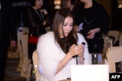 2013年12月郭美美在北京的首饰拍卖会上看手机。这位美女搅动了中国网络和慈善捐款方面的一池春水