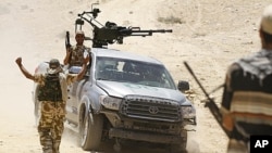 A rebel fighter sitting in a captured Gadhafi forces truck with a mounted weapon is received by comrades occupying high ground overlooking the town of Bir Ghanam, 100 km (62 miles) south of Tripoli, June 30, 2011.