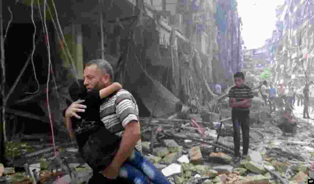In this image made from video and posted online from Validated UGC, a man carries a child after airstrikes hit Aleppo, Syria, April 28, 2016.
