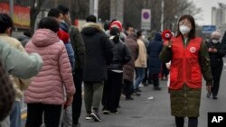 In this photo released by Xinhua News Agency, a volunteer wearing a face mask to protect from the coronavirus uses a loud speaker to give advise to masked residents as they line up for the coronavirus test during a mass testing in north China's Tianjin mu