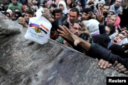 FILE - Syrians who have been evacuated from eastern Aleppo reach out for Russian food aid in the government-controlled Jibreen area in Aleppo, Syria, Nov. 30, 2016.