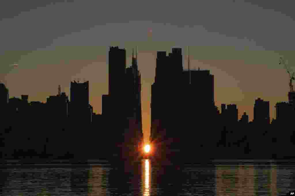 The sun rises through the middle of buildings long 42nd street in New York&#39;s Manhattan borough during a phenomenon known as Manhattanhenge as viewed from Weehawken, New Jersey.