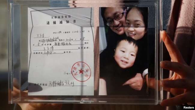资料照：中国维权律师王全璋的妻子李文足手举全家福照片和天津警方的逮捕通知书。（2018年12月17日）