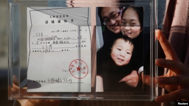 资料照:中国维权律师王全璋的妻子李文足手举全家福照片和天津警方的逮捕通知书。(2018年12月17日)