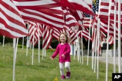 Hazel Roberts walks in a field of flags ahead of Memorial Day, Saturday, May 23, 2020, in Cohasset, Mass. (AP Photo/Michael Dwyer)