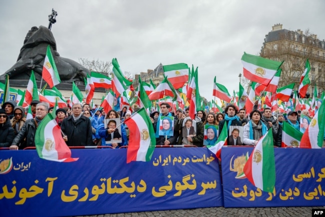 People hold a banner and wave former Iranian flags during a demonstration of the exiled Iranian opposition to protest against the celebration in Iran of the 40th anniversary of the Islamic Revolution, Feb. 8, 2019 in Paris, France.