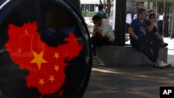 FILE - Residents rest near a map of China posted in a shopping district in Beijing, May 8, 2021. China's overall exports and imports fell by 6.2% in September.