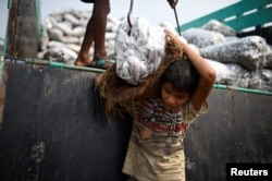FILE - Rohingya refugee Asma Akter, 10, lifts bags of frozen fish from a delivery truck at Nazirartek fish drying yard in Cox's Bazar, Bangladesh, March 23, 2018.