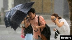 People holding umbrellas walk against strong winds and heavy rain brought by Typhoon Neoguri on a street in Naha, on Japan's southern island of Okinawa, July 9, 2014. 