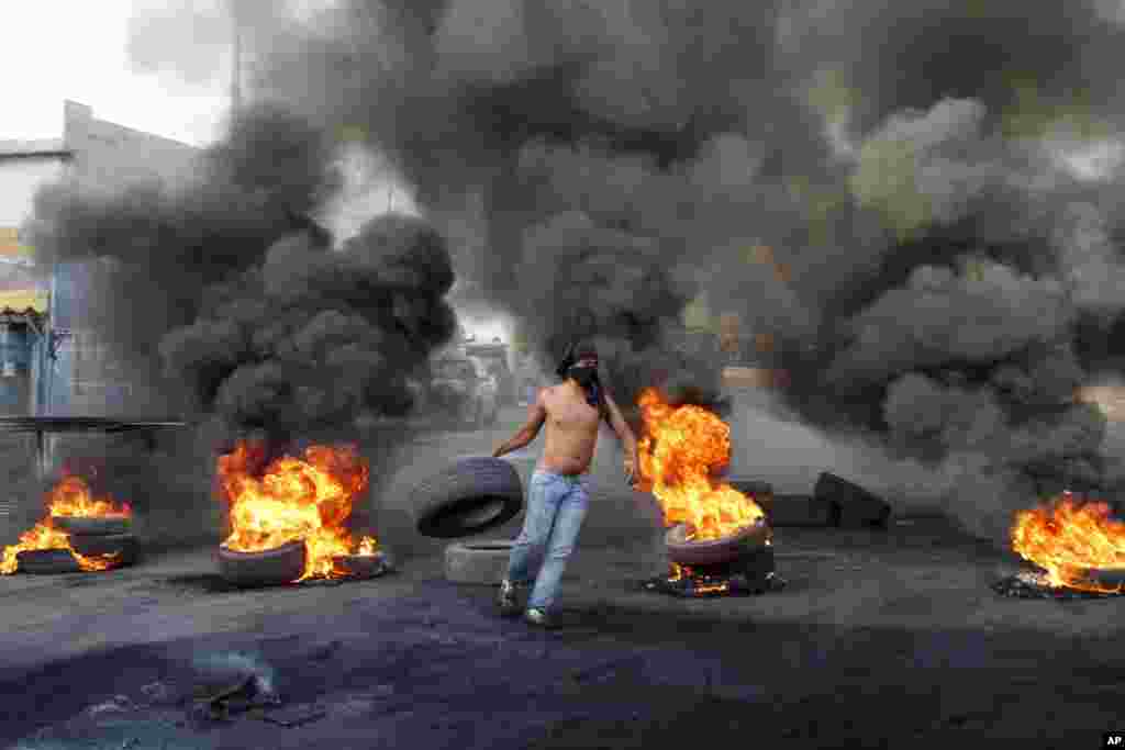 یک تظاهرکننده لاستیکی را به درون آتش می اندازد. تظاهرکنندگان در شهر صیدا به مرگ وسام الحسن دربمب گذاری روز جمعه معترضند. 