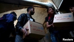Men unload aid boxes from a Red Crescent aid convoy in the rebel held besieged town of Jesreen, Syria, March 7, 2016.