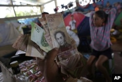 In this March 8, 2018 photo, Venezuelan Charlie Ivan Delgado shows his country's currency as he talks about the economic crisis at a migrant shelter that offers three meals a day where he brought his family of five in Boa Vista, Brazil.