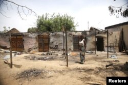 A woman stands in front of a burnt building in Michika town, after the Nigerian military recaptured it from Boko Haram, in Adamawa state, May 10, 2015.