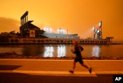 FILE: A jogger runs along McCovey Cove outside Oracle Park in San Francisco, California under darkened skies from wildfire smoke, Sept. 9, 2020.