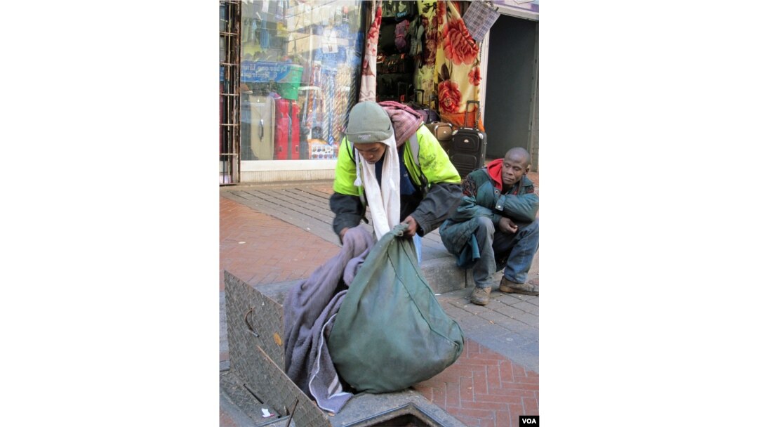 Sello shows his blankets hidden in the drains. His friend Buhlebezwe sits in the background, June 13, 2013 (G. Parker/VOA).